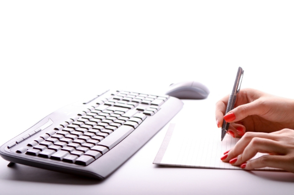 Person writing on pad in front of keyboard